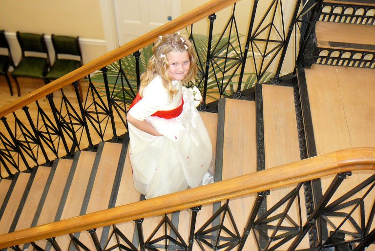 Cute bridesmaid ascends stairs to wedding service. Photo by Isle of Wight wedding photographer JD Photography.